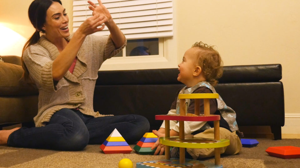 Image of a woman playing with child while sitting on the floor of a living room